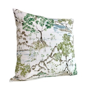 May include: A white cushion with a green and brown watercolour print of trees and mountains. The cushion is made of a soft, textured fabric.