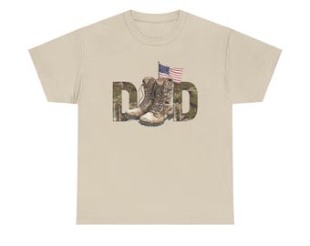 May include: Beige t-shirt featuring the word "DAD" in a camouflage pattern. The letter "A" is replaced with a graphic of combat boots, and a small American flag is positioned above the boots.
