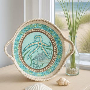 May include: Round decorative tray with a nautical theme. The tray features a rope-like border and handles. The center has a light blue background with an octopus and other sea life. Two seashells are on the table.