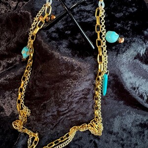 May include: Gold chain glasses holder with turquoise and gold beads. The chain is made of two different styles of gold chain.