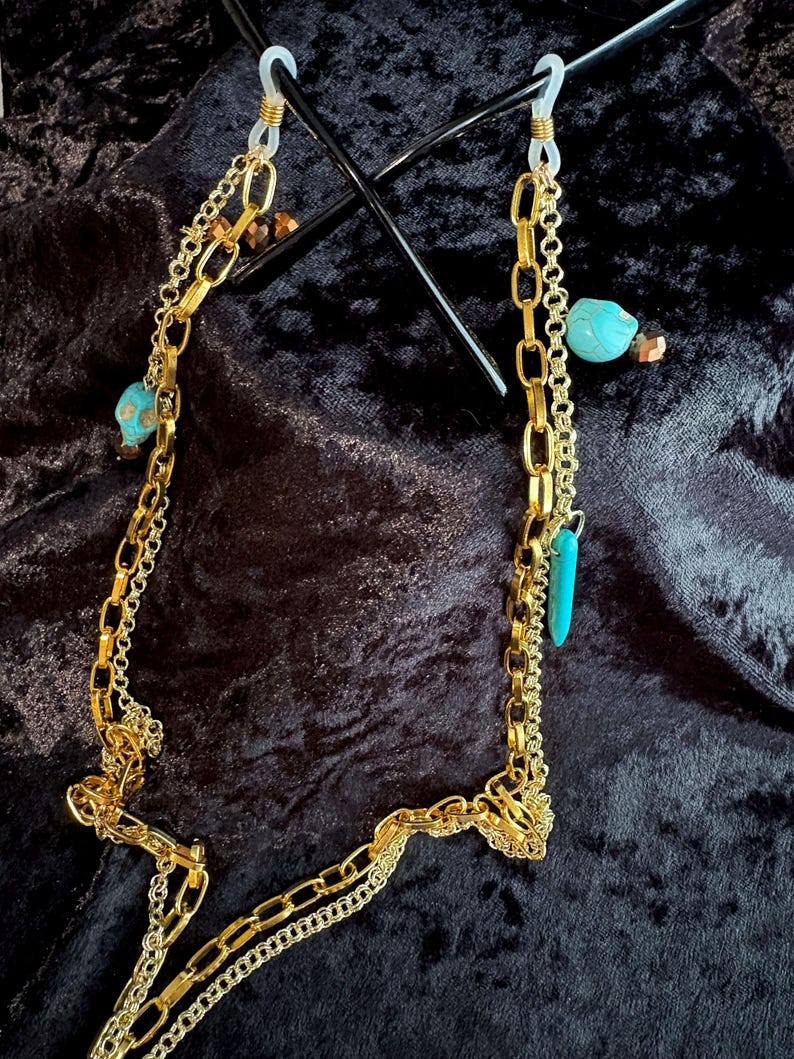 May include: Gold chain glasses holder with turquoise and gold beads. The chain is made of two different styles of gold chain.