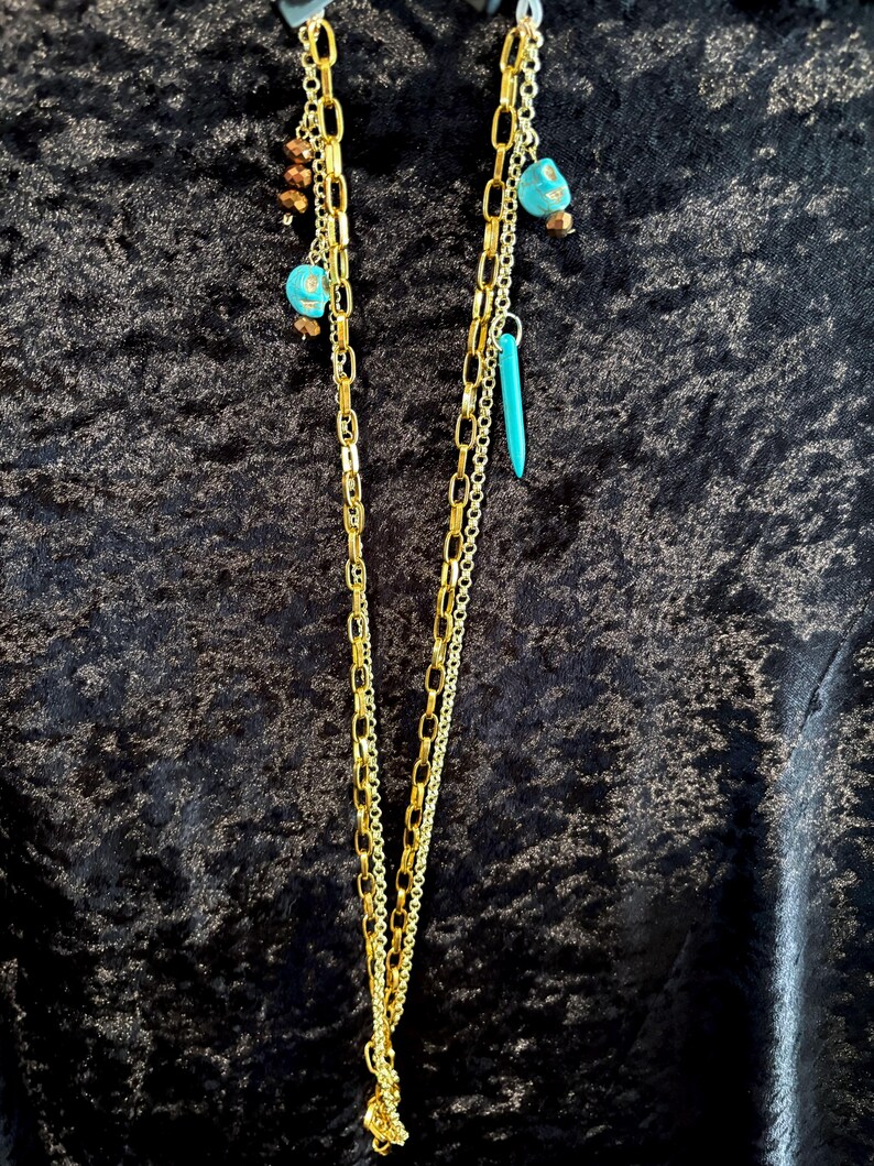 May include: A gold chain necklace with turquoise and brown beads. The necklace has multiple strands of chain and is layered.