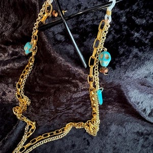 May include: Gold chain glasses holder with turquoise and skull beads. The chain is made of three different styles of gold chain. The chain is attached to clear plastic loops.