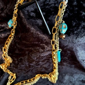 May include: A gold chain with turquoise and gold skull beads, designed to hold glasses.