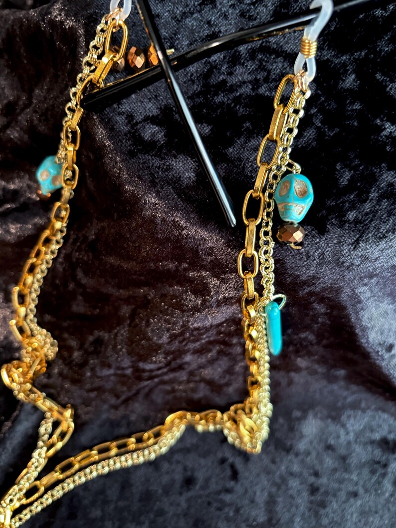 May include: A gold chain with turquoise and gold skull beads, designed to hold glasses.