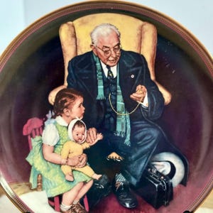 May include: A round decorative collector plate featuring a Norman Rockwell illustration of an older person in a dark suit and glasses sitting in a yellow chair, holding a pocket watch, with a child holding a doll sitting on their lap.