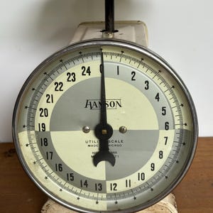 May include: Vintage Hanson utility scale with a black top and a round face. The face has a white and gray color scheme with black numbers and a black needle. The scale is marked with the Hanson name and "Utility Scale Chicago".