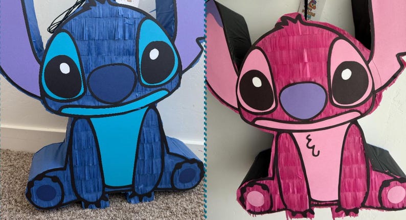 May include: Two pi&ntilde;atas shaped like the cartoon character Stitch. One is blue with light blue details, the other is pink with black accents. Both have large ears, big eyes, and a friendly expression. They are made of paper and are likely for a party or celebration.