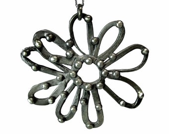 May include: A silver-toned metal pendant shaped like a flower with eight looped petals. The surface features small, raised spherical studs along the edges and center. The pendant hangs from a thin, delicate silver-toned metal chain.