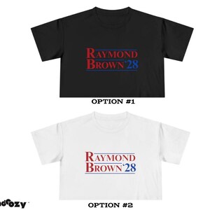 May include: Two t-shirts, one black and one white, each featuring the text "RAYMOND BROWN 28" in red and blue. The shirts are displayed with the option numbers #1 and #2 below them. The brand name "trendcozy" is in the bottom left corner.