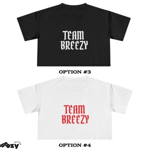 May include: Two cropped t-shirts, one black and one white, each with the text "TEAM BREEZY" in a gothic font. The black shirt has white text, and the white shirt has red text. The shirts are displayed against a white background.