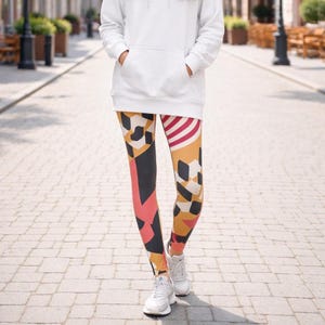 May include: Leggings with a colorful geometric pattern. The leggings feature a mix of black, orange, red, and white shapes. The person is wearing white sneakers and a white hoodie.