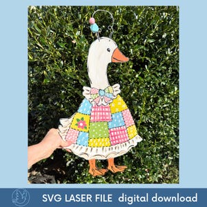 May include: A wooden goose decoration with a white head, orange beak, and a patchwork quilt-style dress in pastel colors. The goose has a decorative bow and a wire with beads on top. The text "SVG LASER FILE digital download" is at the bottom.