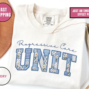 May include: Ivory t-shirt featuring the words "Progressive Care UNIT" in blue, floral-patterned letters. The shirt has a crew neck and short sleeves. The text "JUST AN EMBROIDERY EFFECT PRINT" is also visible.