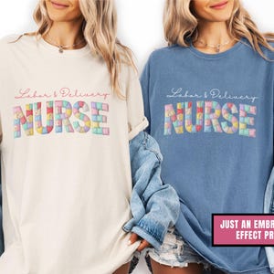 May include: Two t-shirts, one cream and one blue, each with the words "Labor & Delivery Nurse" in script. The word "NURSE" is in a colorful patchwork design. A pink rectangle at the bottom right says "JUST AN EMBROIDERY EFFECT PRINT".