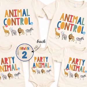 Pu&ograve; includere: T-shirt e body color crema con testo colorato e grafica di animali. Le magliette riportano "ANIMAL CONTROL" e "PARTY ANIMAL" con illustrazioni di giraffa, elefante, leone e zebra. Un cerchio mostra il numero 2.