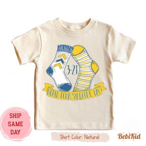 May include: Cream-coloured t-shirt with a graphic of two socks, one white with blue details and the other yellow with stripes. The design includes the date "3-21" and the text "World Down Syndrome Day" on a yellow banner.