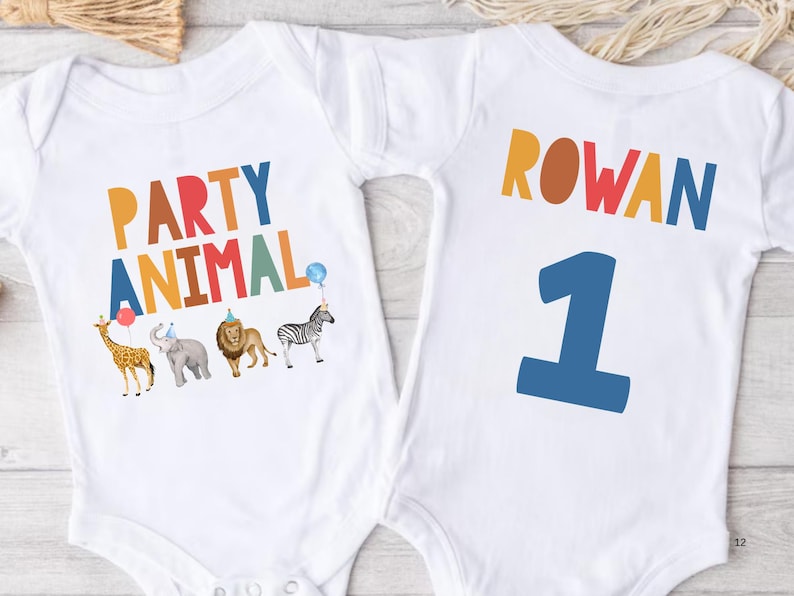 Pu&ograve; includere: Body per neonati bianco con le parole "PARTY ANIMAL" in lettere colorate e illustrazioni di animali. Il retro del body ha il nome "ROWAN" e il numero "1" in blu.