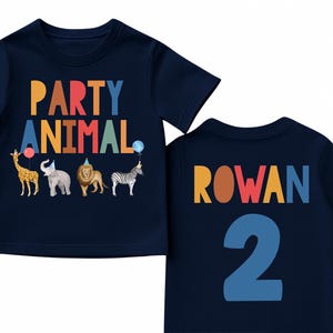 Pu&ograve; includere: T-shirt blu navy per bambini piccoli con la scritta "PARTY ANIMAL" in lettere colorate e illustrazioni di animali. Il retro della maglietta mostra il nome "ROWAN" e il numero "2" in una combinazione di colori coordinata.