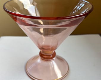 May include: A pink glass cocktail or martini glass with a gold rim. The glass has a wide, flared bowl and a tall, slender stem.