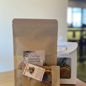 May include: A holiday simmering potpourri set in a kraft paper bag, with a white gift box. The set includes dried orange slices, cinnamon sticks, and other ingredients. The packaging includes the text "Holiday Simmering Potpourri".