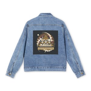 May include: A light blue denim jacket with a graphic on the back. The graphic shows three alien figures and the words "HUMAN RESEARCH". The design uses beige, brown, and gold. The jacket has a classic design with button closures and pockets.