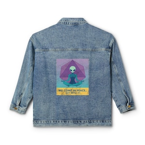 Könnte beinhalten: Hellblaue Jeansjacke mit einer Grafik eines Aliens, das unter einer violetten geometrischen Form meditiert. Der Text "WE COME IN PEACE... GET WITH IT!" ist unter dem Alien-Bild aufgedruckt. Die Jacke hat einen klassischen Kragen und Knöpfe.