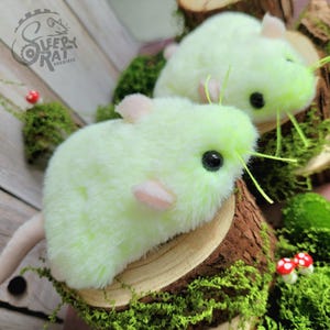 Peut inclure: Deux rats en peluche avec une fourrure vert clair, de petites oreilles roses et des yeux noirs. Chaque rat est posé sur une tranche de bois circulaire décorée de mousse verte et de petits champignons rouges et blancs. Un logo indique Sleepy Rat Archives.