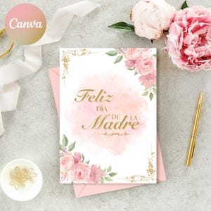 May include: A white card with a pink watercolor background and gold lettering that says "Feliz Dia de la Madre". The card is decorated with pink flowers and gold accents.