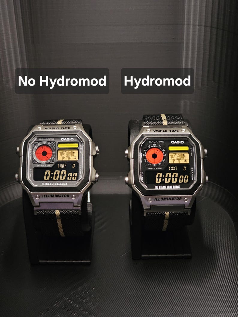 May include: Two digital Casio watches side-by-side, one labeled "No Hydromod" and the other "Hydromod." Both watches have a silver case, black band with yellow stripe, and a digital display showing "0:00 00." The text "ILLUMINATOR" is visible.