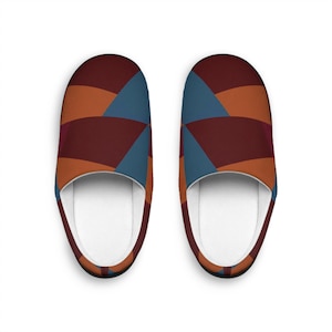 May include: A pair of slip-on slippers featuring a geometric pattern of overlapping curved shapes in deep burgundy, burnt orange, and slate blue. The interior of the slippers is lined with a solid white fabric, providing a clean contrast to the exterior.