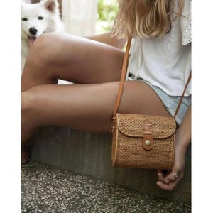 May include: A brown woven crossbody bag with a leather strap and buckle closure. The bag is made of natural materials and has a simple, elegant design.