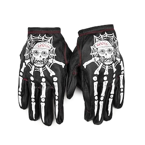 May include: A pair of black leather gloves with a white skeleton hand and skull design. The skull is wearing a hat that says "Wasted".