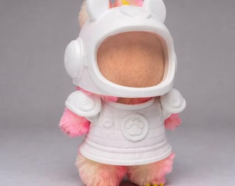 May include: A plush toy astronaut, featuring a white helmet and space suit. The toy is predominantly pink and yellow, with yellow feet. The helmet has ear-like features. The space suit has paw print details.