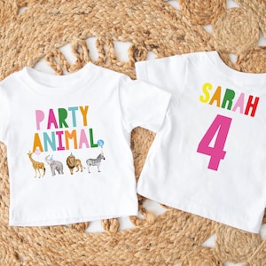 May include: Two white t-shirts with colorful graphics. One says "PARTY ANIMAL" with animal illustrations. The other says "SARAH 4". The shirts are likely for a birthday party or celebration.