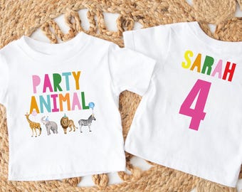 May include: Two white t-shirts with colorful graphics. One says "PARTY ANIMAL" with animal illustrations. The other says "SARAH 4". The shirts are likely for a birthday party or celebration.