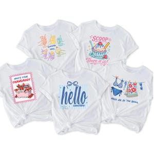 May include: Five white t-shirts with summer-themed graphics. Designs include cocktails, ice cream, a crawfish box, the words "hello sunshine", and beach attire. Each shirt has a knotted front.
