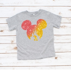 Puede incluir: Una camiseta gris con una silueta brillante de Mickey Mouse en rojo y amarillo. El dise&ntilde;o incluye un castillo y Mickey Mouse. La camiseta est&aacute; hecha de un material suave y es adecuada para ni&ntilde;os.