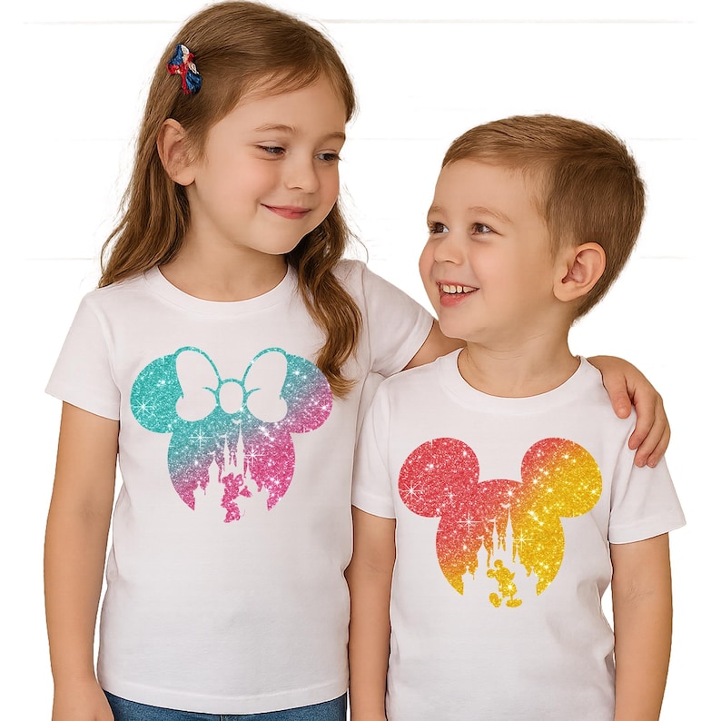 Puede incluir: Dos ni&ntilde;os con camisetas blancas con dise&ntilde;os brillantes de colores. Una camiseta presenta una silueta de Minnie Mouse turquesa, rosa y morada con un castillo. La otra camiseta tiene una silueta de Mickey Mouse roja, naranja y amarilla con un castillo y Mickey.