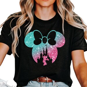 Puede incluir: Camiseta negra con silueta brillante de Minnie Mouse en tonos azules y rosas. El dise&ntilde;o incluye un castillo y un lazo, creando un efecto caprichoso y brillante. Prenda de vestir informal.