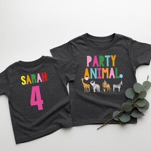 May include: Two dark gray t-shirts. One says "SARAH 4" in colorful letters. The other says "PARTY ANIMAL" above animal illustrations, including a giraffe, elephant, lion, and zebra, each with party accessories.