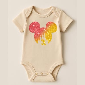 Puede incluir: Body de beb&eacute; color crema con una silueta brillante de Mickey Mouse en tonos rojos, naranjas y amarillos. El dise&ntilde;o incluye una silueta de castillo y estrellas. El body tiene mangas cortas y cierres de broche.