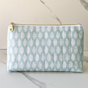 May include: A light blue zippered pouch with a white floral pattern. The pouch has a gold zipper and a gold pull tab.