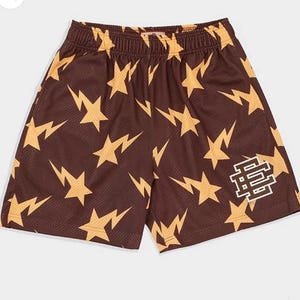 Op de afbeelding: Bruine basketbalshorts met een patroon van gele sterren en bliksemschichten. De shorts hebben een wit "8 & 8" logo op het rechterbeen.