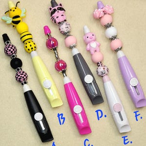 May include: A set of three ceramic mugs with a speckled, cream-colored glaze. Each mug features a different hand-painted design: a blue and green leaf, a yellow flower, and a red berry. The mugs have a simple, modern design.