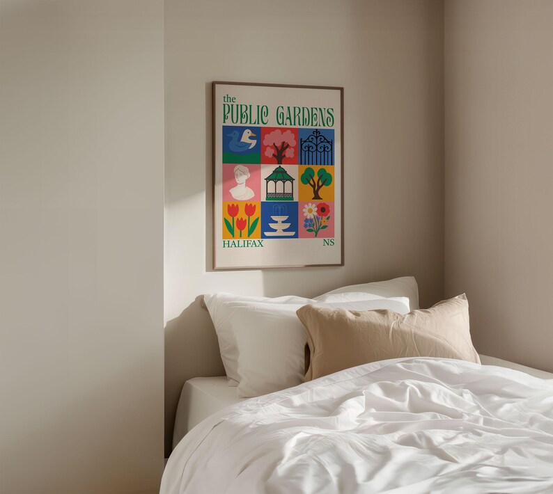 Op de afbeelding: Een ingelijste poster getiteld "The Public Gardens" met kleurrijke vierkante illustraties. Het kunstwerk toont een vogel, boom, poort, buste, tuinhuisje, bloemen en het woord "Halifax". De poster wordt weergegeven boven een bed met wit beddengoed.