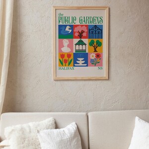 Op de afbeelding: Een ingelijste kunstafdruk getiteld "The Public Gardens" met kleurrijke illustraties van een zwaan, boom, poort, buste, prieel, boom, tulpen, fontein en bloemen. De print zit in een licht houten frame.