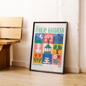 Op de afbeelding: Een ingelijste poster getiteld "The Public Gardens" met kleurrijke illustraties van een eend, boom, poort, buste, tuinhuisje, boom, tulpen, fontein, bloem en de tekst "Halifax NS". De poster leunt tegen een witte muur.