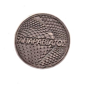 May include: A circular, silver-coloured coin with the Greek inscription "ΑΠΑΡΑΒΙΑΤΟΣ" across its centre. The coin's surface has a textured pattern, possibly representing scales or a similar design. The word is in capital letters.