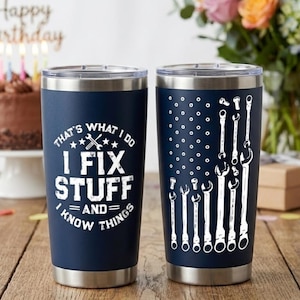 May include: Two navy blue stainless steel tumblers with silver rims. One tumbler has the text "THAT'S WHAT I DO, I FIX STUFF, AND I KNOW THINGS" in white. The other has a white wrench design.